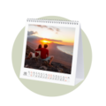 A couple sits on a cliff watching the sunset over the sea, accompanied by a CEWE photo calendar featuring this image.